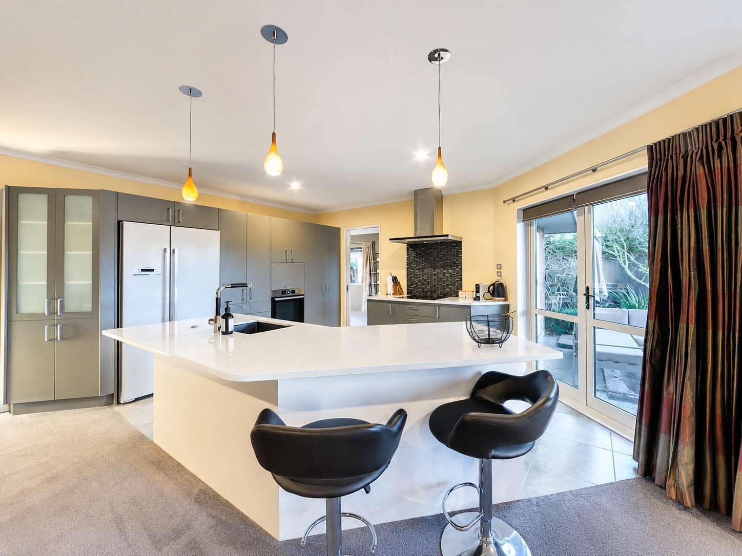 A modern kitchen with a central island, two bar stools, and pendant lighting.