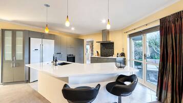 A modern kitchen with a central island, two bar stools, and pendant lighting.