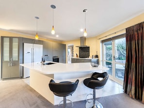 A modern kitchen with a central island, two bar stools, and pendant lighting. - Spacious 4BR Retreat | Halswell Domain Park & Lake (Christchurch)