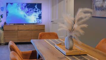 A dining area with a wooden table, chairs, a vase with feathers, and a television in the background.