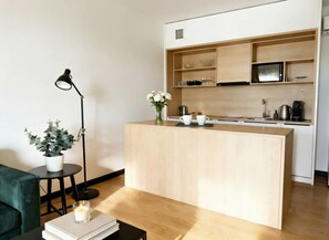 Eine moderne Küche mit Holzschränken, einer zentralen Kochinsel und einem Essbereich mit einem grünen Sofa und einem kleinen Tisch mit Kerze.