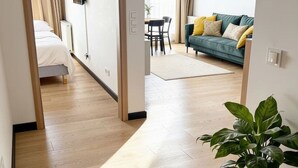 Habitación de hotel con piso de madera, una cama, un televisor, un comedor y un sofá verde con almohadones.