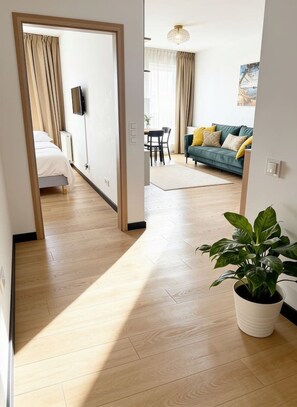 Ein Hotelzimmer mit Holzboden, einem Bett, einem Fernseher, einem Essbereich und einem grünen Sofa mit Kissen.