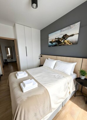 Um quarto moderno com uma cama grande, cabeceira, mesa de cabeceira e um quadro na parede.
