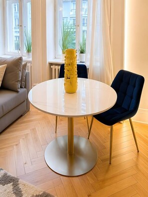 Ein runder Tisch mit einer gelben Vase, einem blauen Stuhl und einem Sofa in einem gut beleuchteten Raum mit Holzboden.