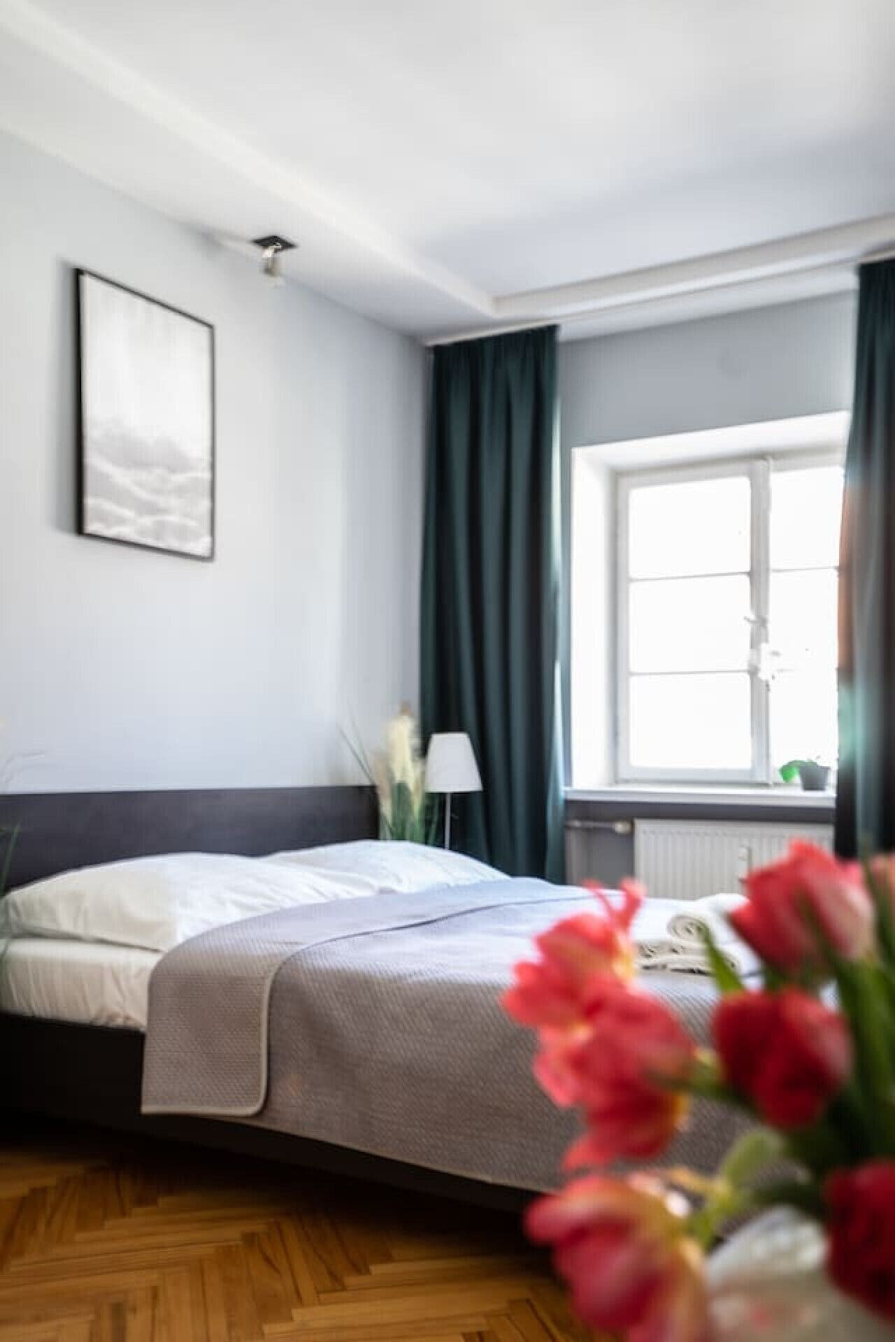 Een slaapkamer met een bed, een raam met gordijnen, een bedlampje en een aan de muur hangend schilderij.