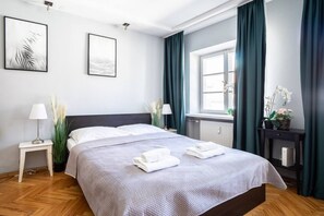 Une chambre d’hôtel bien aménagée, avec un lit, des lampes de chevet, une fenêtre avec des rideaux et des œuvres d’art accrochées au mur.
