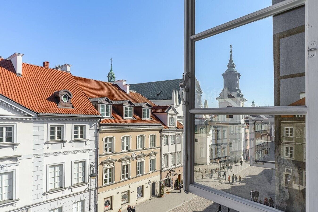 Une vue d’une rue bordée de bâtiments historiques, un ciel dégagé et un reflet dans une fenêtre.