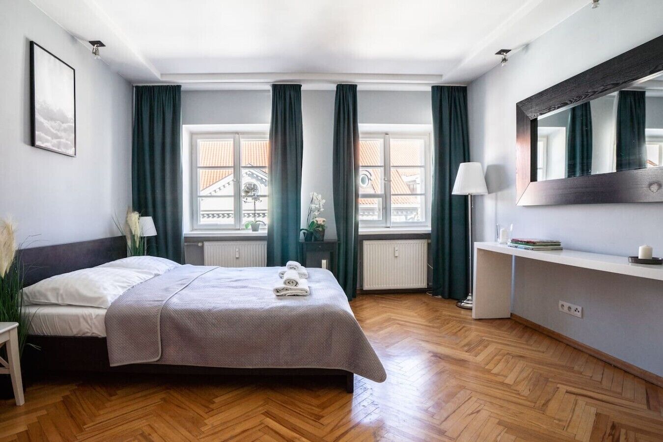 Une chambre d’hôtel avec un lit, une table de chevet, une lampe, un miroir et une fenêtre avec des rideaux.