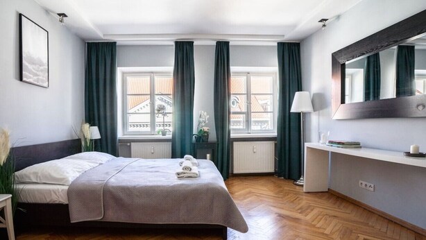 Ein Hotelzimmer mit Bett, Nachttisch, Lampe, Spiegel und einem Fenster mit Vorhängen.