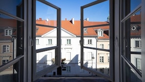 Blick durch ein offenes Fenster auf ein Gebäude mit roten Ziegeldächern und weißen Fassaden.