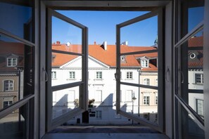 Blick durch ein offenes Fenster auf ein Gebäude mit roten Ziegeldächern und weißen Fassaden.