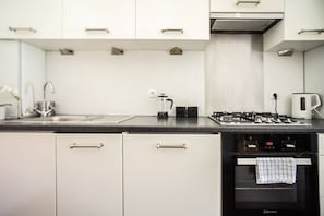 A modern kitchen with white cabinets, a stainless steel sink, a gas stove, and a built-in oven. - OldTownHeart XVII -Freta Luxury (Warsaw)