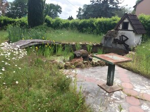 A garden with a stone bridge, a small house-like structure, and a paved walkway.