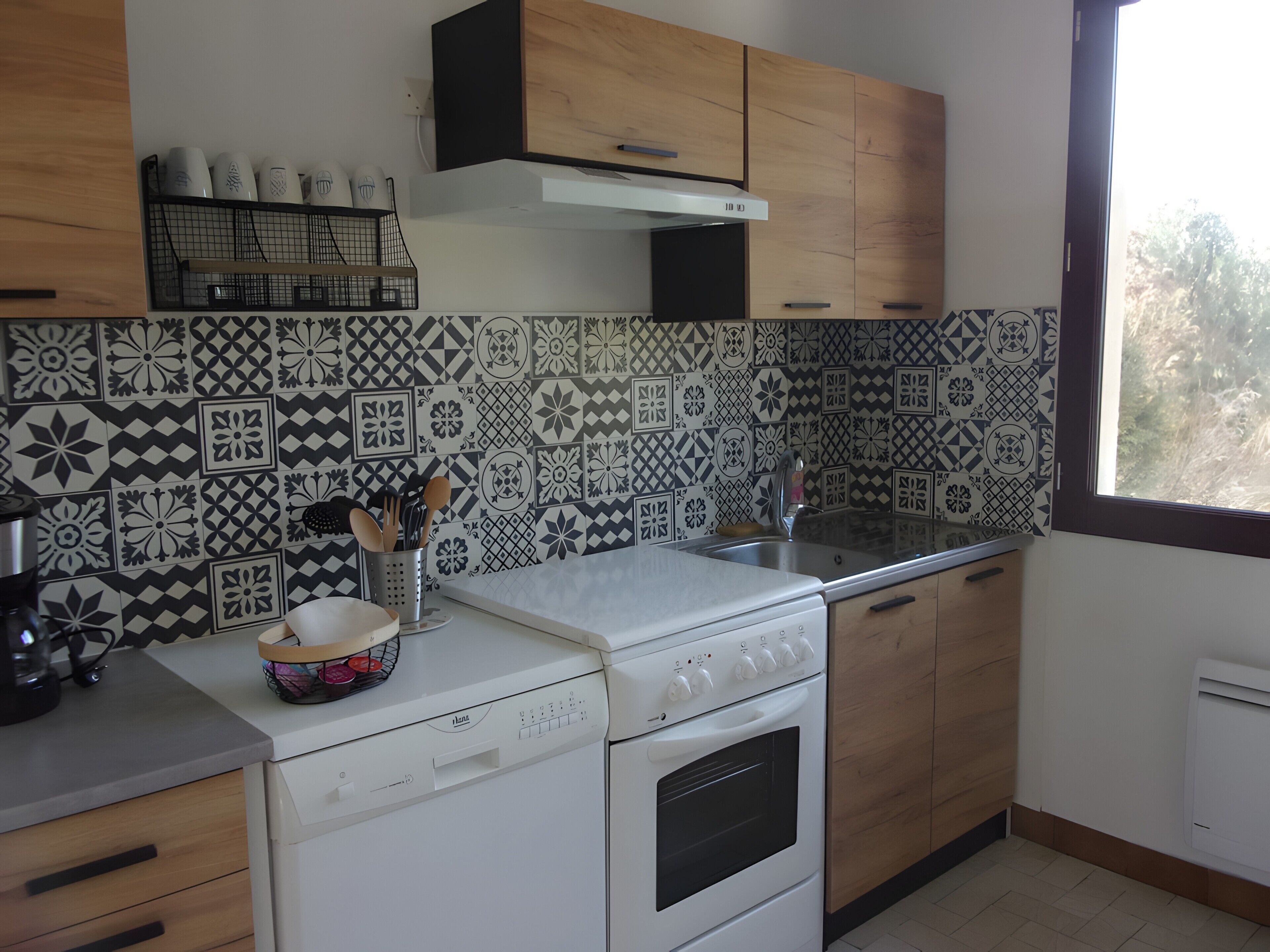 A kitchen with patterned tiles, wooden cabinets, a dishwasher, and a window with a view.