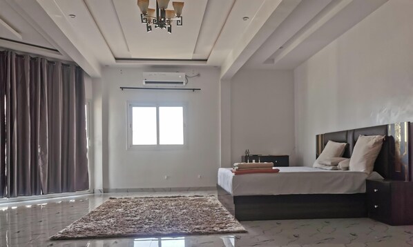 A modern bedroom with a large bed, a headboard, a bedside table, and a window.