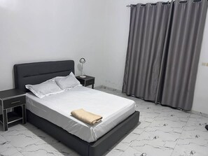 Een bed met wit beddengoed, een nachtkastje, een lamp en een grijze gordijn.