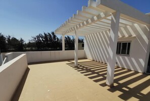A covered outdoor area with a tiled floor, white walls, and a pergola structure.