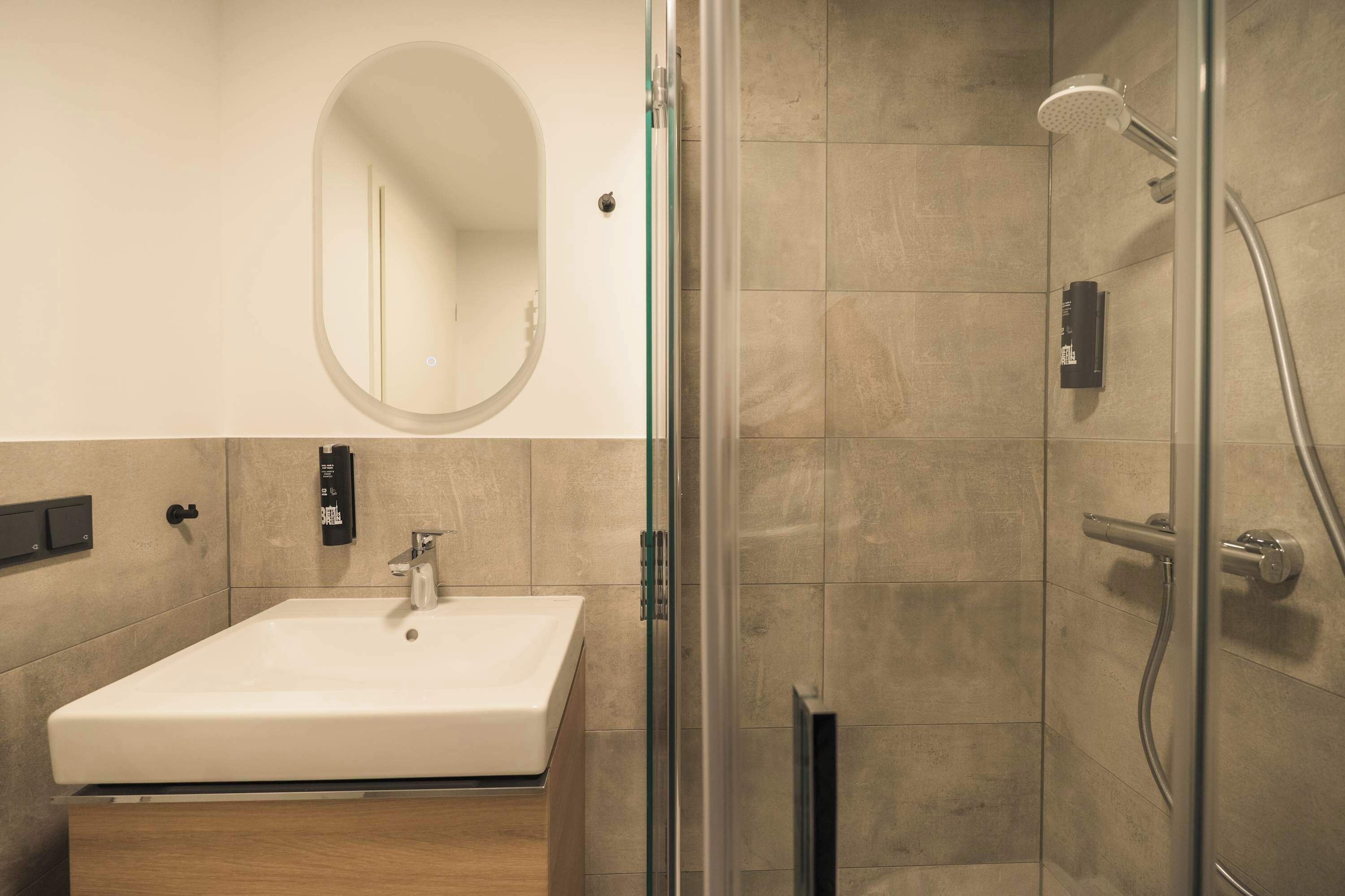 Un baño moderno con ducha envuelta en vidrio, un lavabo blanco y un espejo grande.