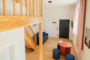 Ein Zimmer mit einer Holztreppe, einem Sofa, einer Tür und einem kleinen Tisch mit Hockern.