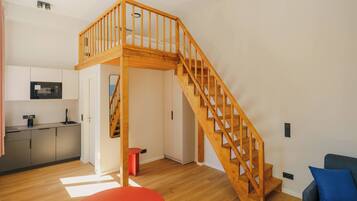 Un espacio habitable moderno con una escalera de madera que lleva a una zona superior, una cocina con microondas y un taburete rojo.