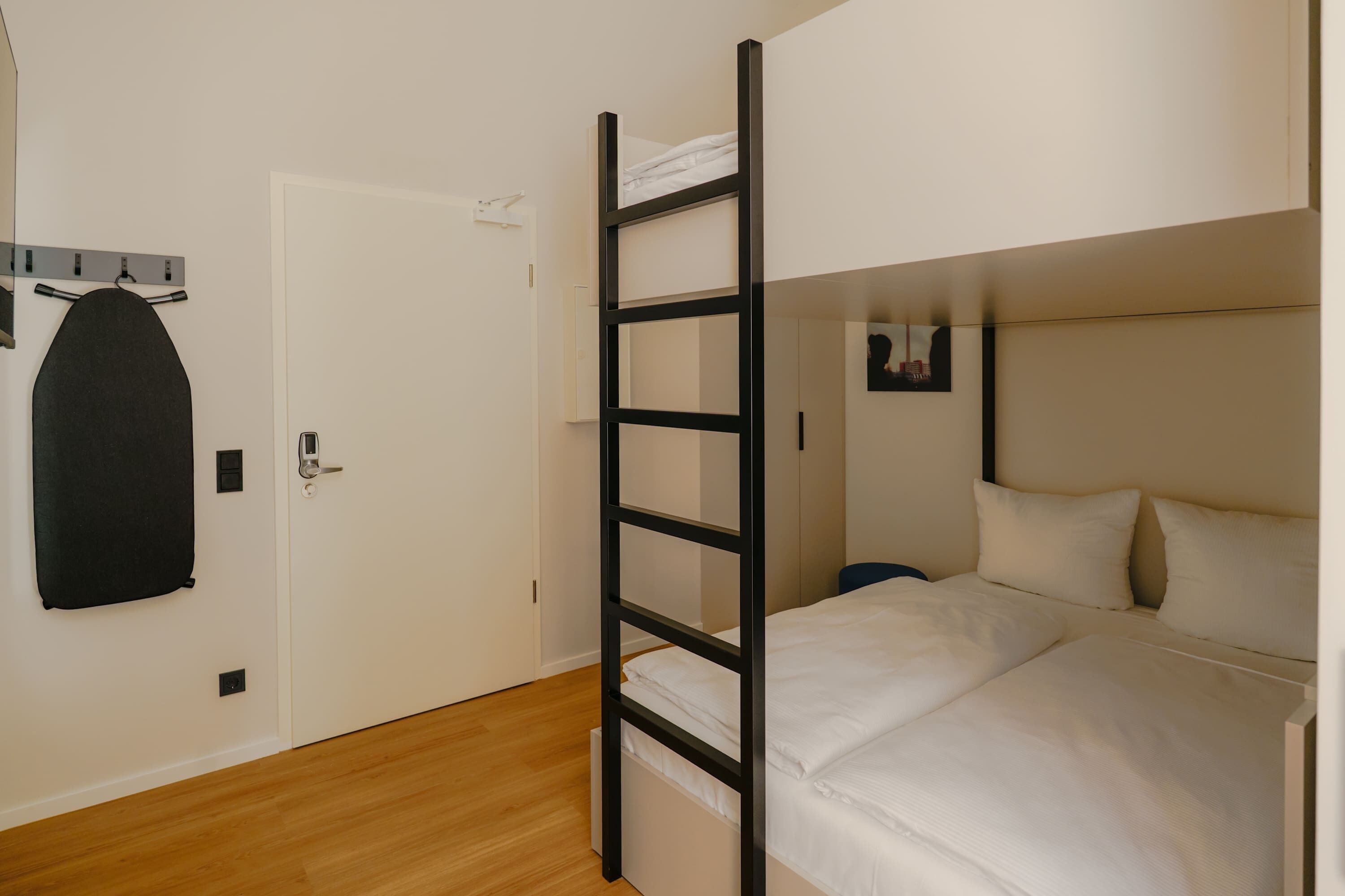 Habitación pequeña con una litera, un perchero en la puerta y una mesita de noche.