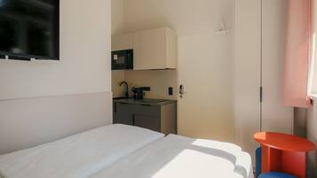 Una habitación de hotel con una cama, una mesita, un microondas y un armario.