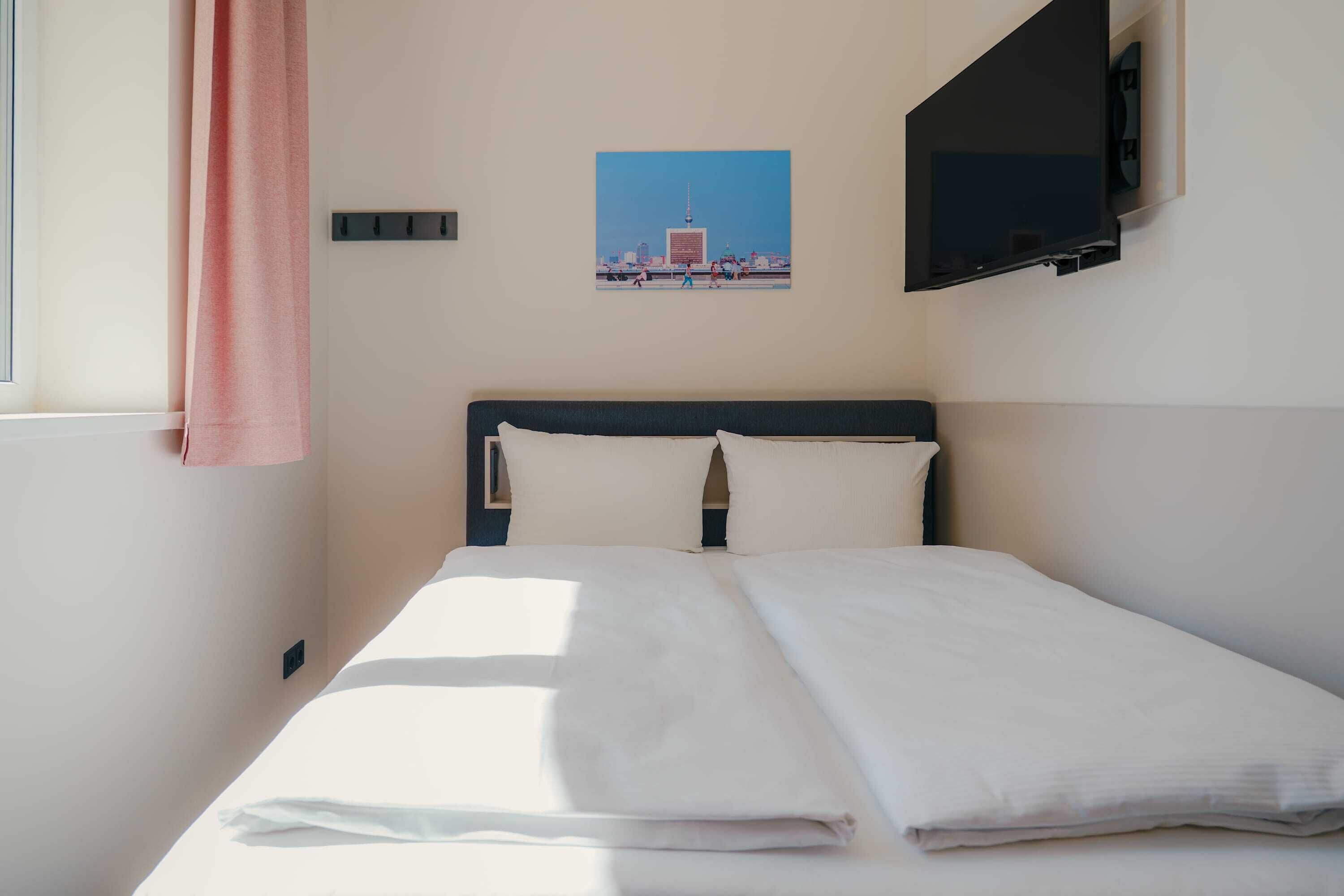 Una habitación de hotel con una cama, un televisor en la pared y una ventana con cortina.