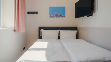 Una habitación de hotel con una cama, un televisor en la pared y una ventana con cortina.