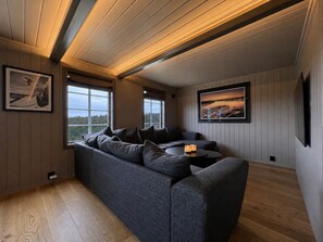 A modern living room with a sectional sofa, two windows, a flat-screen TV, and a framed landscape painting. - Modern and Homey Apartment near slopes in Kikut, Geilo (Hol)