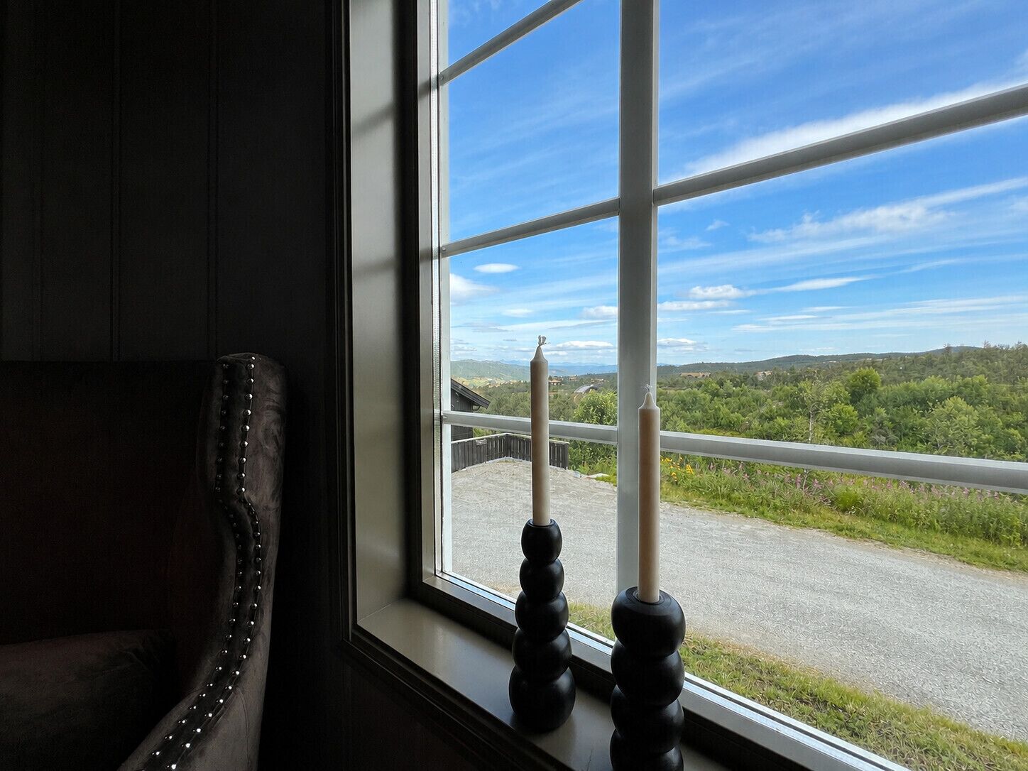 Habitación con vista a una carretera y vegetación, visible a través de una ventana con marco metálico.