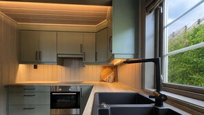 Una cocina moderna con electrodomésticos integrados, un lavamanos negro y una ventana con vistas a zonas verdes.