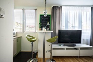 A compact living space with a kitchenette, a flat-screen TV, and two green bar stools. - Old Town Heart XXI- Pl.Teatralny (Warsaw)