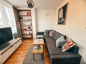 A modern living room with a flat-screen TV, a grey sofa, a wooden coffee table, and a bookshelf. - Old Town Heart XXI- Pl.Teatralny (Warsaw)