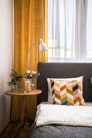 A hotel room with a bed, a bedside table with a lamp, a potted plant, and a window with curtains. - Old Town Heart XXI- Pl.Teatralny (Warsaw)