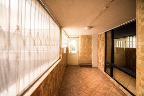 Un pasillo con suelo de baldosas, una puerta al final y una ventana a la izquierda.