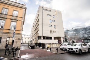 A multi-story building with a parking garage entrance, a bicycle parked outside, and several cars parked in front. - Old Town Heart XXI- Pl.Teatralny (Warsaw)