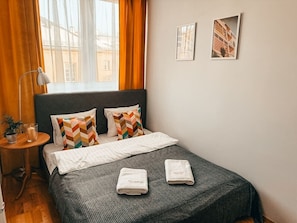 Una cama bien hecha con dos almohadas, una mesita de noche con una lámpara y dos cuadros enmarcados en la pared.