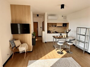 Ein modernes Wohnzimmer mit Fernseher, einer Sitzecke, einem Esstisch und einer Küche im Hintergrund.
