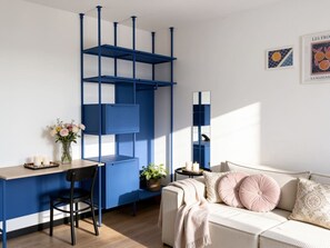Ein Zimmer mit einem blauen Bücherregal, einem Schreibtisch mit Stuhl, einer Couch mit Kissen und einem kleinen Tisch mit Kerzen.