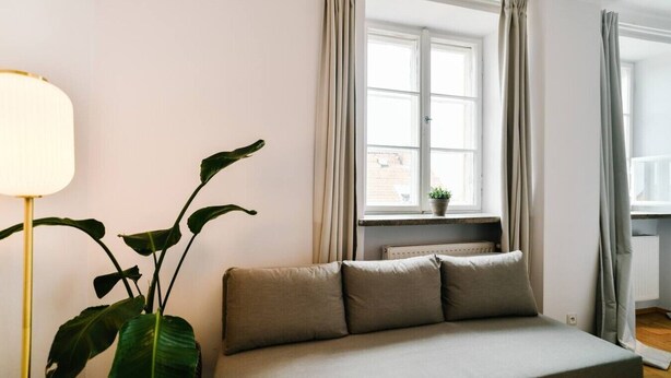 Um quarto com uma cama, uma janela com cortinas, um radiador e um vaso de plantas.