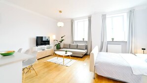 Quarto de hotel moderno com cama, sofá, mesa de jantar, televisão e janela com cortinas.
