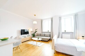 Ein modernes Hotelzimmer mit Bett, Sofa, Esstisch, Fernseher und einem Fenster mit Vorhängen.