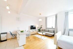 Un salon moderne avec un canapé, un coin repas comprenant une table et des chaises, un téléviseur et une grande fenêtre avec des rideaux.