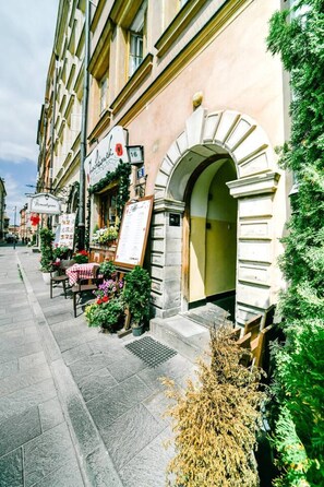 Straßenansicht eines Gebäudes mit Bogenportal, Außenbereich mit Tischen und Stühlen sowie einem Schild.
