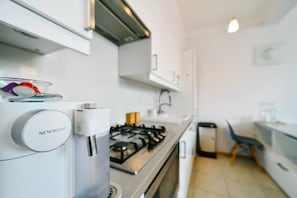 A modern kitchen with a built-in espresso machine, a gas stove, and a small dining area with a chair. - Old Town Heart V - Old Town Square (Warsaw)