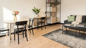 En moderne stue med et rundt spisebord, sorte stole, et sort sofabord, en grå sofa, et sort reolsystem og en potteplante.