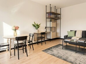 Ein modernes Wohnzimmer mit einem runden Esstisch, schwarzen Stühlen, einem schwarzen Couchtisch, einem grauen Sofa, einer schwarzen Regaleinheit und einer Topfpflanze.