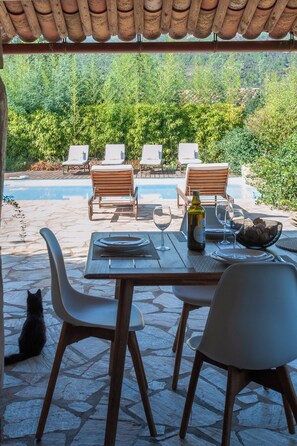 Ein Essbereich im Freien mit Pool, Holzstühlen und einem Steintisch.