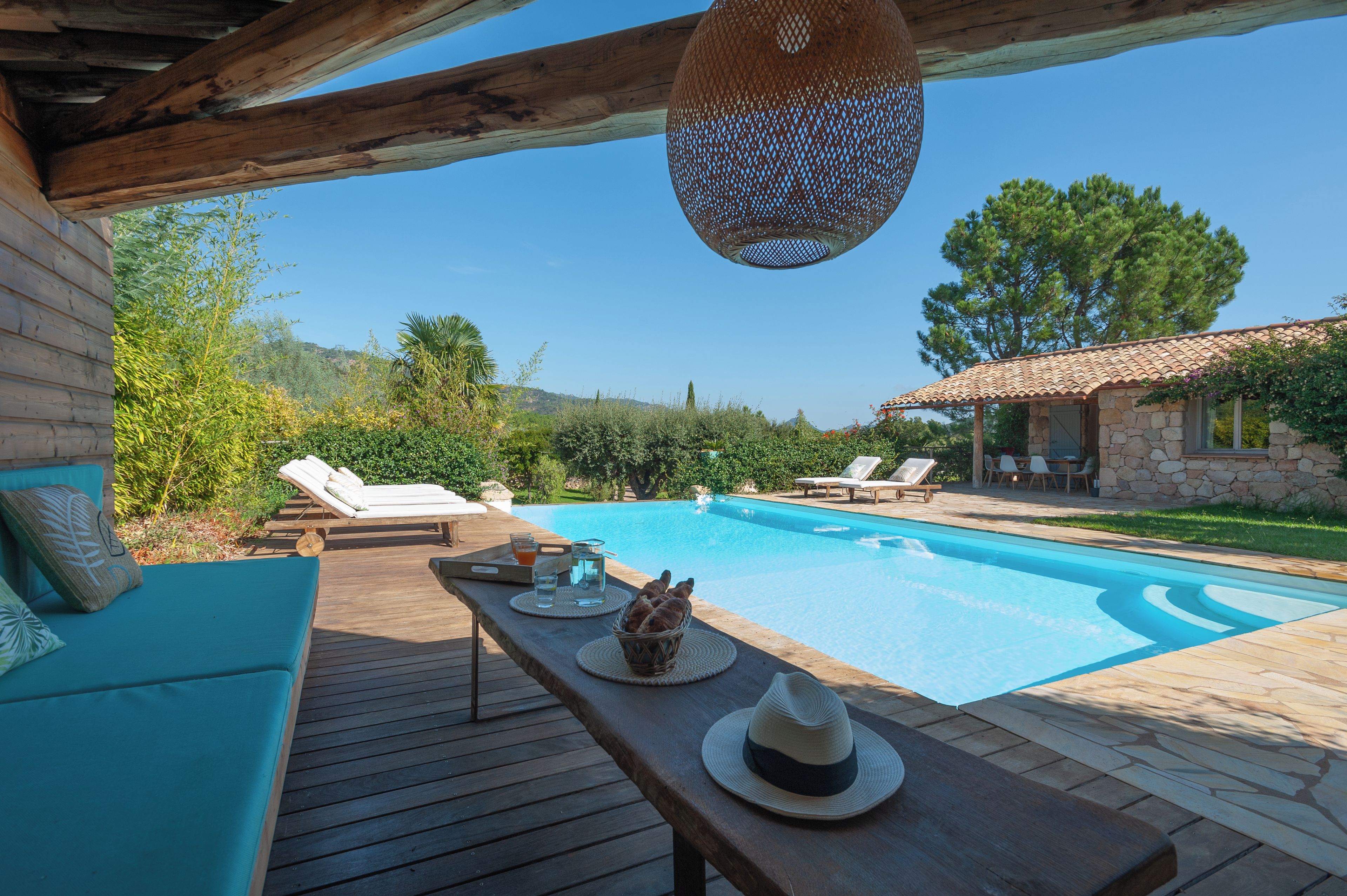 A wooden deck with a pool, lounge chairs, and a stone building with a tiled roof.